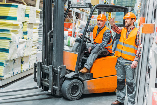worker and his senior colleague working with forklift machine in storage