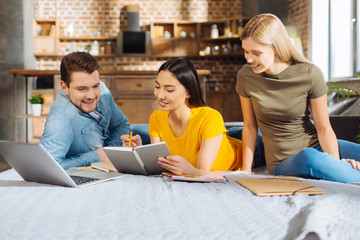 Team work. Three gay merry positive friends looking at the notebook while smiling and communicating