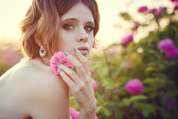 Beautiful young woman in a blooming rose garden