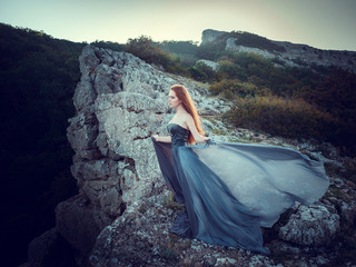 Summer outdoors portrait of beautiful furious scandinavian warrior ginger woman in grey dress with...