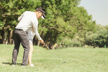 Plakat Asian couple playing golf. man teaching woman to play golf while standing on field