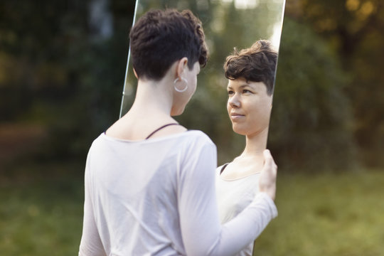 Smiling woman with short hair looking in mirror while standing at park