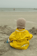 baby boy in yellow rain coat plays on the beach