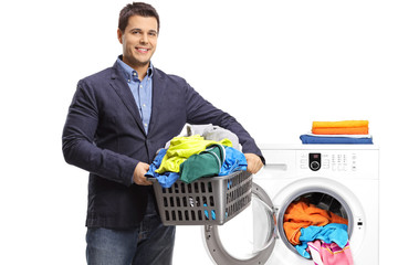 Elegant guy holding a laundry basket filled with clothes in front of a washing machine