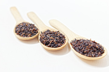 Thai Black or dark brown raw rice in a wooden spoon for a healthy diet. High fiber, vitamin, carbohydrate, minerals, and nutrition for healthy people. on the white background, isolate.