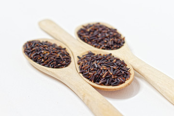 Thai Black or dark brown raw rice in a wooden spoon for a healthy diet. High fiber, vitamin, carbohydrate, minerals, and nutrition for healthy people. on the white background, isolate.