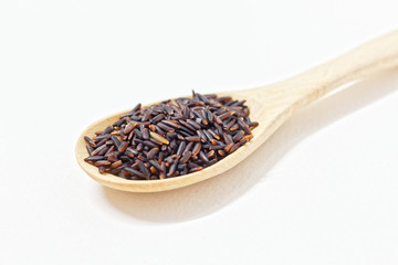 Thai Black or dark brown raw rice in a wooden spoon for a healthy diet. High fiber, vitamin, carbohydrate, minerals, and nutrition for healthy people. on the white background, isolate.