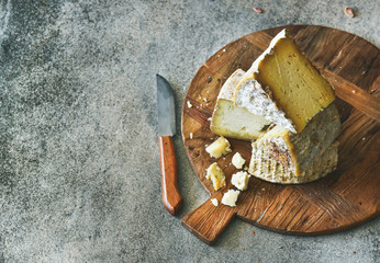 Cheese platter with cheese assortment on wooden board over grey concrete background, selective focus, copy space. Party or gathering eating concept