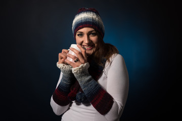 Woman holding a cup while wearing a warm hat and a sweater