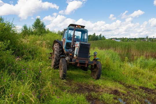 The tractor stands in the tall grass on the shore of the pond