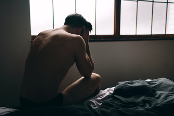 Depressed man sitting on bed in an empty room , This is major depressive disorder