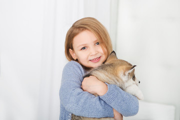 Happy Little girl lying on a bed and hugging with the puppy husky dog