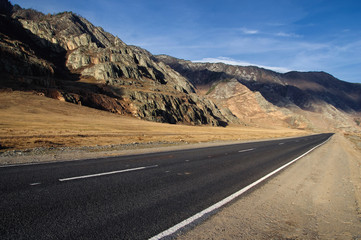 Road asphalt path on a desert wild mountain valley yellow dry grass at the background of the high ranges under a blue sky Chuysky tract Altai Mountains Siberia, Russia