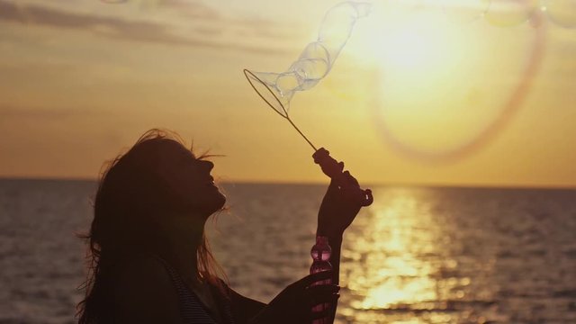 Smiling woman blowing soap bubbles on the beach at wonderful sunset in slow motion. 1920x1080