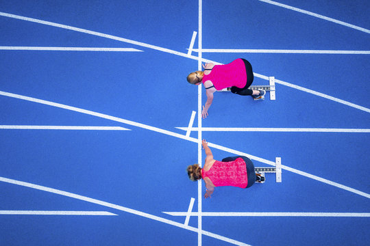 Top view of two female runners starting on tartan track