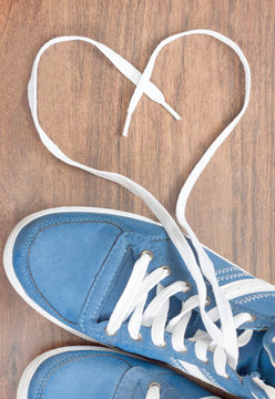 blue shoes with unbound lace in the shape of a heart on a wooden floor