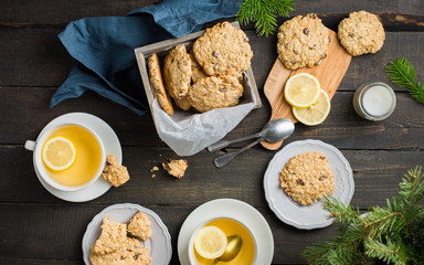 The perfect tasty breakfast!)  Oatmeal cookies with chocolate in wooden box and green tea with lemon in mugs on a dark background with a Xmas tree. Best useful Cookies.  Flat lay, top view