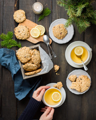 The perfect tasty breakfast!)  Oatmeal cookies with chocolate in wooden box and green tea with lemon in mugs on a dark background with a Xmas tree. Best useful Cookies.  Flat lay, top view