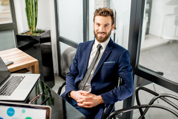 Portrait of a handsome banker working with laptop sitting at the luxury office interior - obrazy, fototapety, plakaty