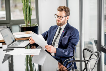 Portrait of a handsome banker working with laptop sitting at the luxury office interior with...
