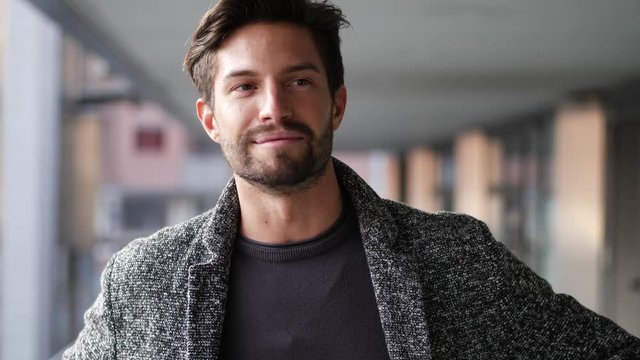 One handsome young man in urban setting in European city, standing, smiling and talking to the camera