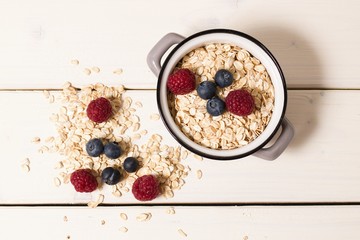 Top down view on small pot full of oatmeal, fresh raspberies and blueberries