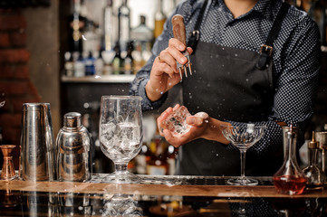 Barman crushing a big piece of ice for making a cocktail