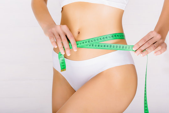 woman dressed in white underwear measures her slim stomach. concept ideal body, sport training and diet.