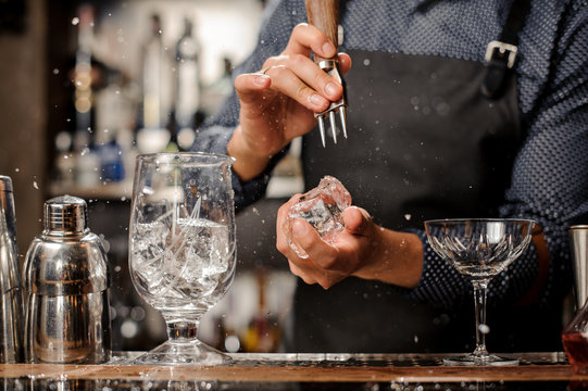 Bartender crushing a big piece of ice for a cocktail