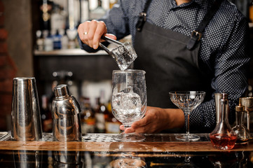 Barman putting a big ice cube with help of special ice tongs