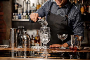 Barman putting a big ice cube into the glass with help of special ice tongs