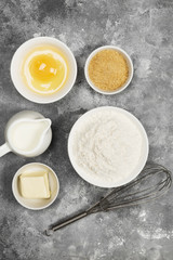 Ingredients for pastries - flour, eggs, butter, milk, sugar on a gray background. Top view. Food background