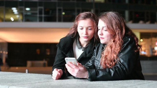 two young women outdoor city night using smart phone - internet, social network, technology concept