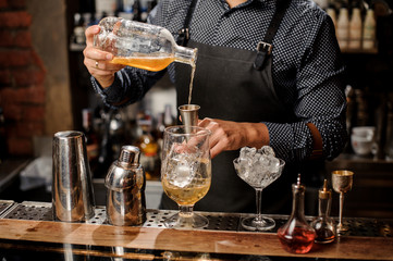 Bartender pouring syrup into the large cocktail glass