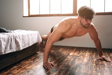 Naked bearded dark-hair man doing push-up exercise home morning.