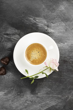 Espresso coffee in a white cup, a pink rose and chocolates on a dark background. Top view. Food background