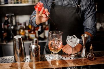 Bartender pouring red sweet fruit syrup into the large cocktail glass