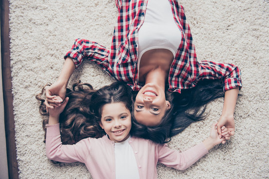 Friendly relationship between mother and her little daughter. Top view photo of smiling relatives lying on the floor and holding hands, they have long beautiful dark hair