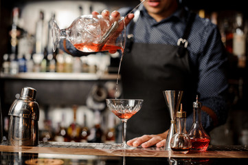 Barman pouring red alcoholic drink into the cocktail glass