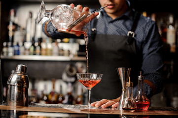 Bartender pouring red alcoholic drink into the cocktail glass