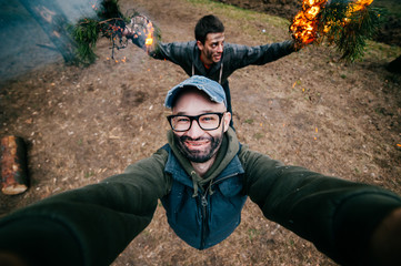 Frineds make selfie. Crazy funny boys mess around. Men at nature playing dangerous fire games....