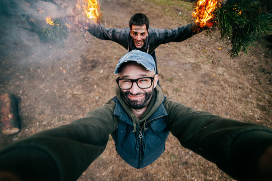 Frineds make selfie. Crazy funny boys mess around. Men at nature playing dangerous fire games. Eccentric bizarre strange unusual young guys with dirty faces mad party in forest. Burn, flame, smoke.