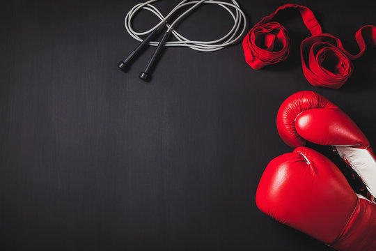 Professional red boxing gloves, wraps, and skipping rope on black background with copy space.