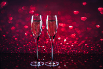 Two glasses of champagne with red heart shape bokeh on background.