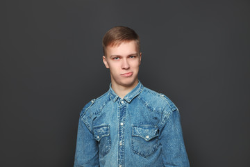 Portrait of young handsome man in jeans shirt looking at camera over dark grey background. Emotions and facial expressions concept.