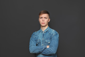 Obraz premium Portrait of young handsome man in jeans shirt looking at camera over dark grey background. Emotions and facial expressions concept.