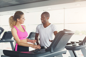 Fitness instructor helps young woman on treadmill