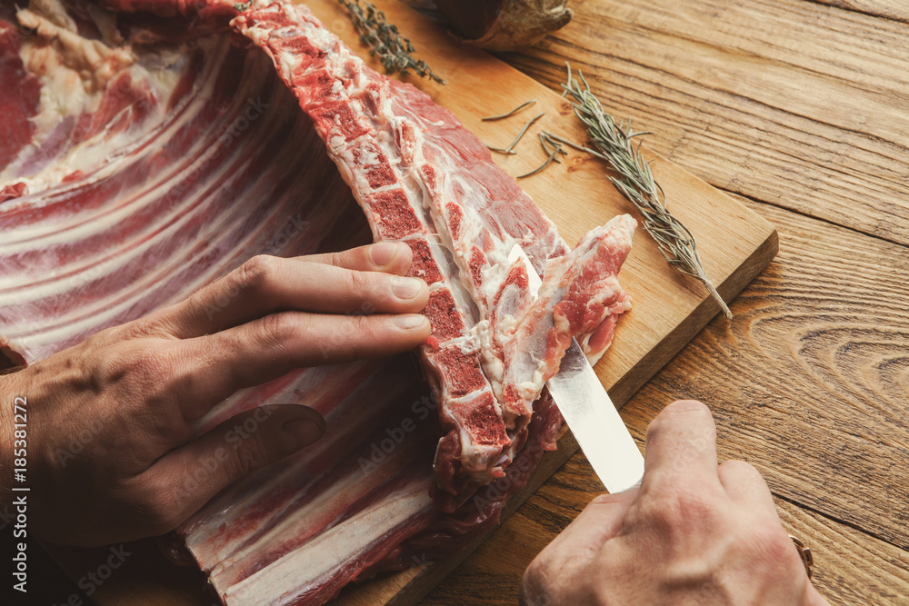 Wall mural chef cutting rack of lamb on wooden board in kitchen