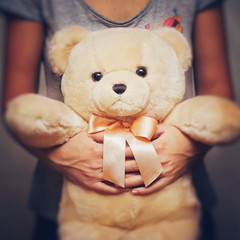 A girl is holding and hugging a teddy bear. Concept idea - goodbye to childhood. Vintage style