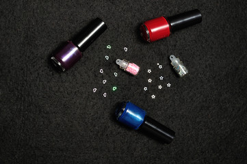 Bottles of nail polish with nail decorations displayed on a black background